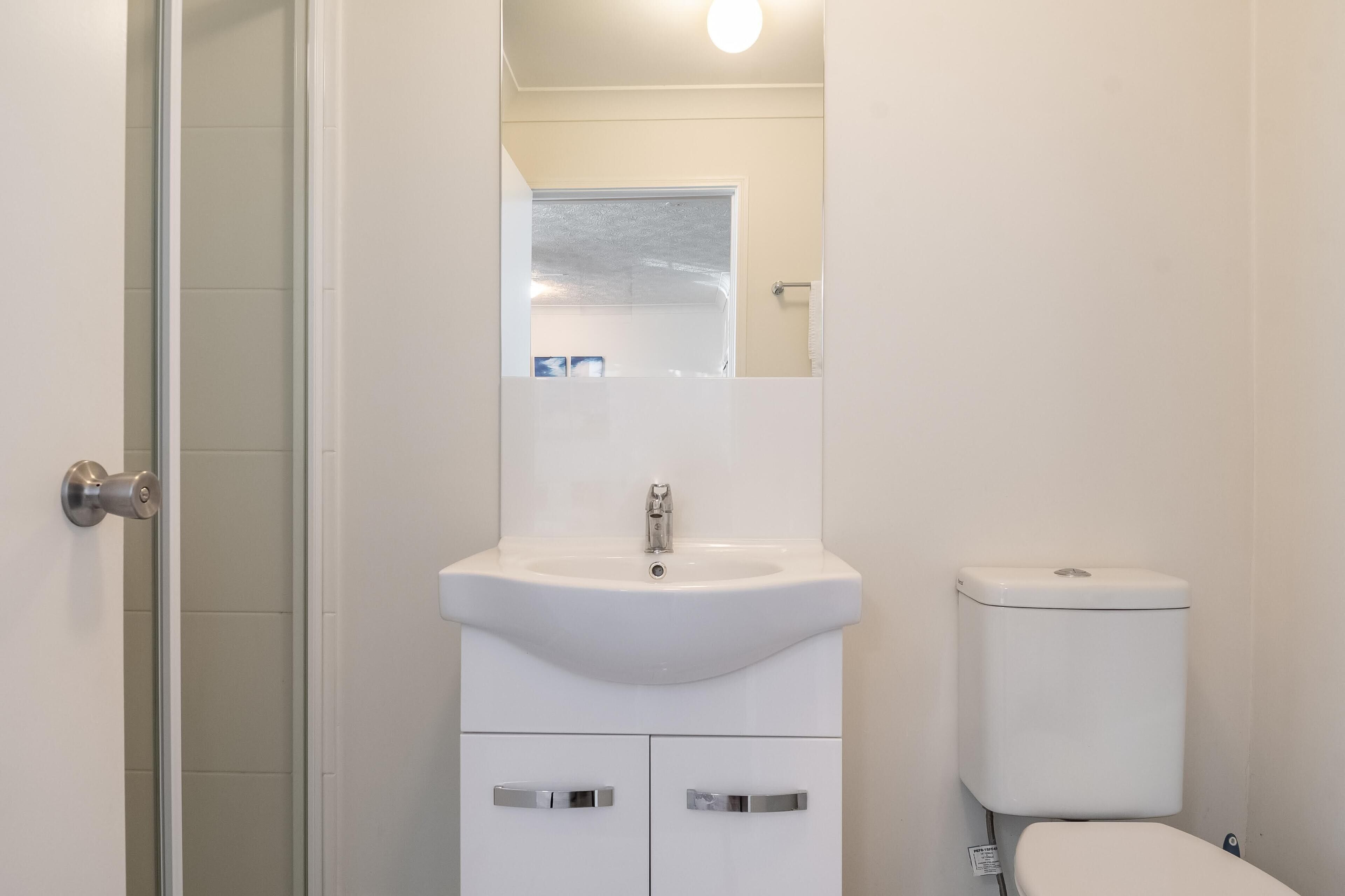 A bathroom with a white sink, mirror, and toilet.