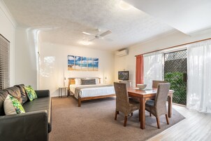 Una habitación de hotel moderna con una cama, un sofá, una mesa de comedor con sillas, un ventilador de techo y un gran ventanal con cortinas.