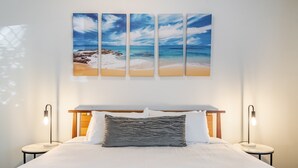 A hotel room with a bed, two bedside lamps, a nightstand, and a wall-mounted artwork of a beach scene. - Byron Central Apartments (Byron Bay)