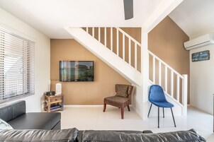 Una sala de estar con una escalera, un sofá, un sillón y un televisor.