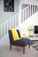 Un salón moderno con un sillón gris, un plaid amarillo, una mesita con un jarrón de flores y una escalera al fondo.