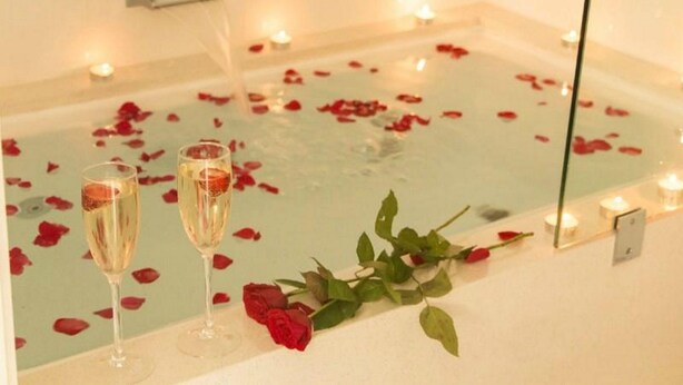 A bathtub with rose petals and candles, suggesting a romantic setting. - Byron Central Apartments (Byron Bay)