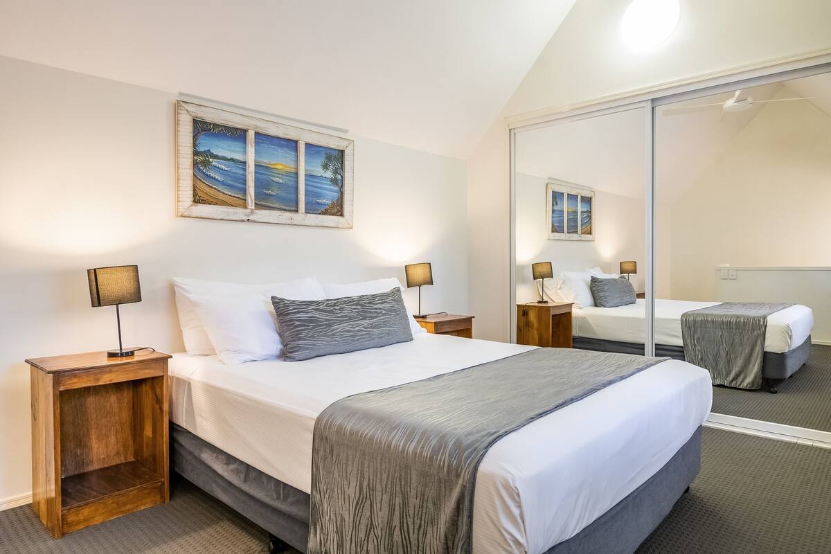 A bedroom with a large bed, bedside tables, a mirror, and a painting on the wall.