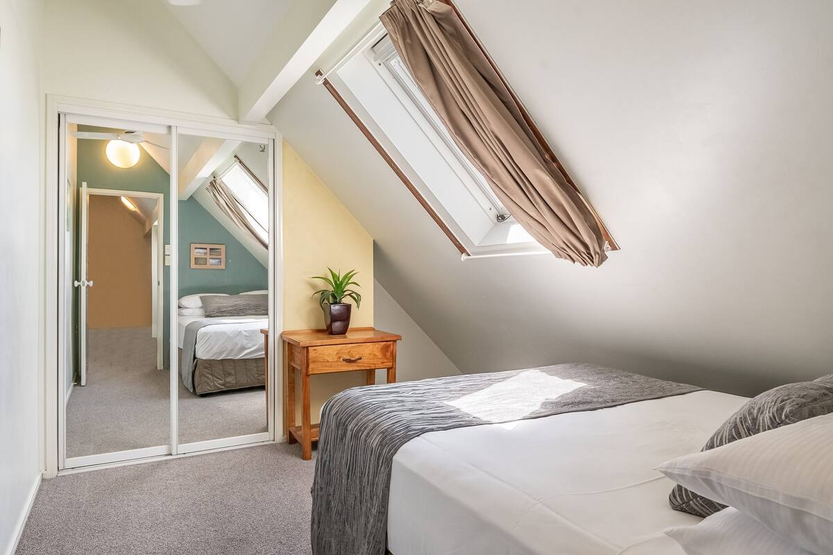 A bedroom with a bed, a bedside table with a plant, a sliding door leading to another room, and a skylight.