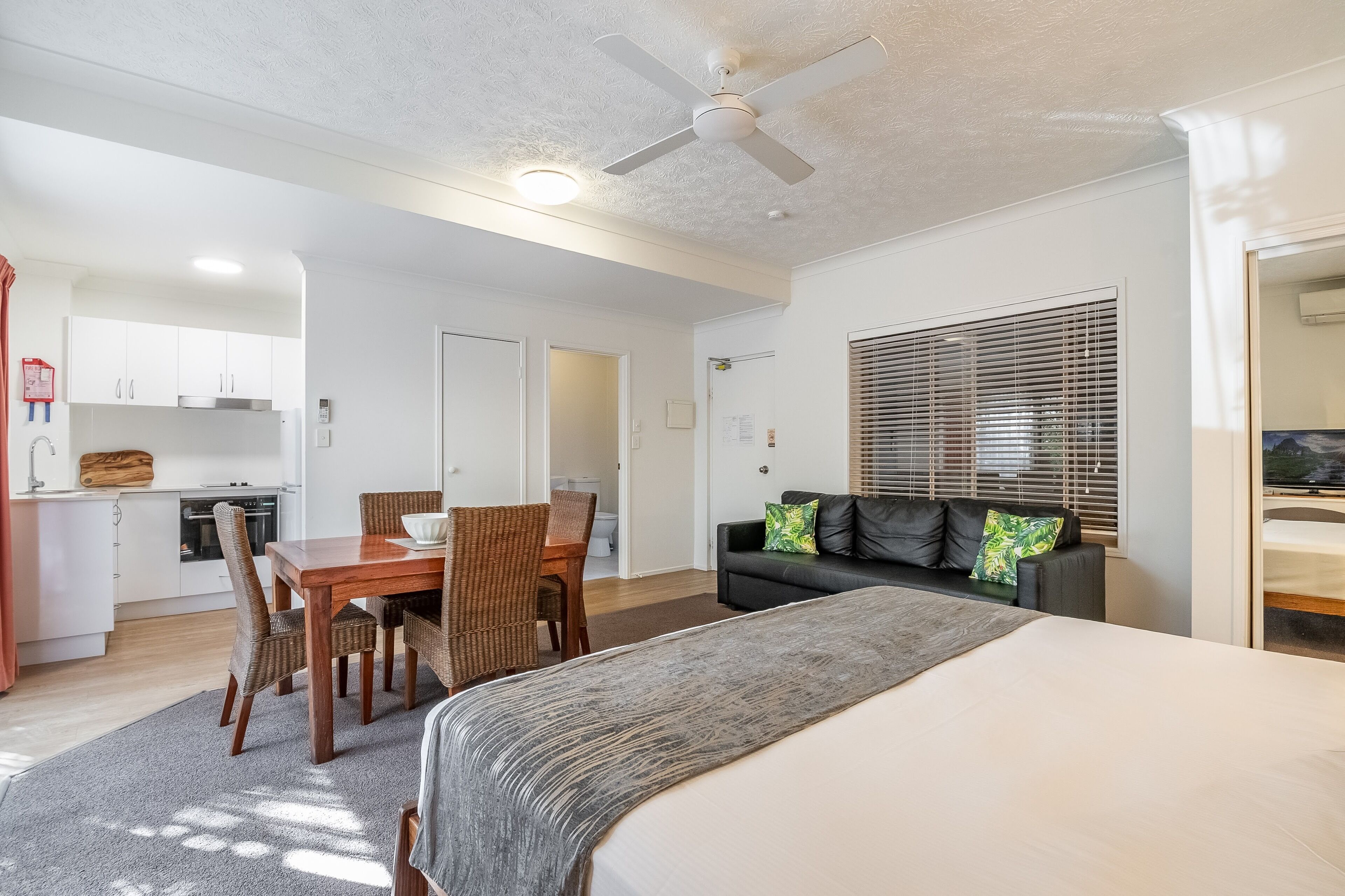 A modern, well-lit room with a bed, a dining table with chairs, a sofa, and a kitchen area.