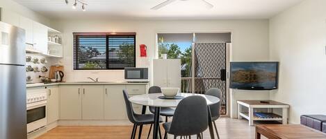 A modern kitchen with white cabinets, a dining table with chairs, a TV, and a ceiling fan.