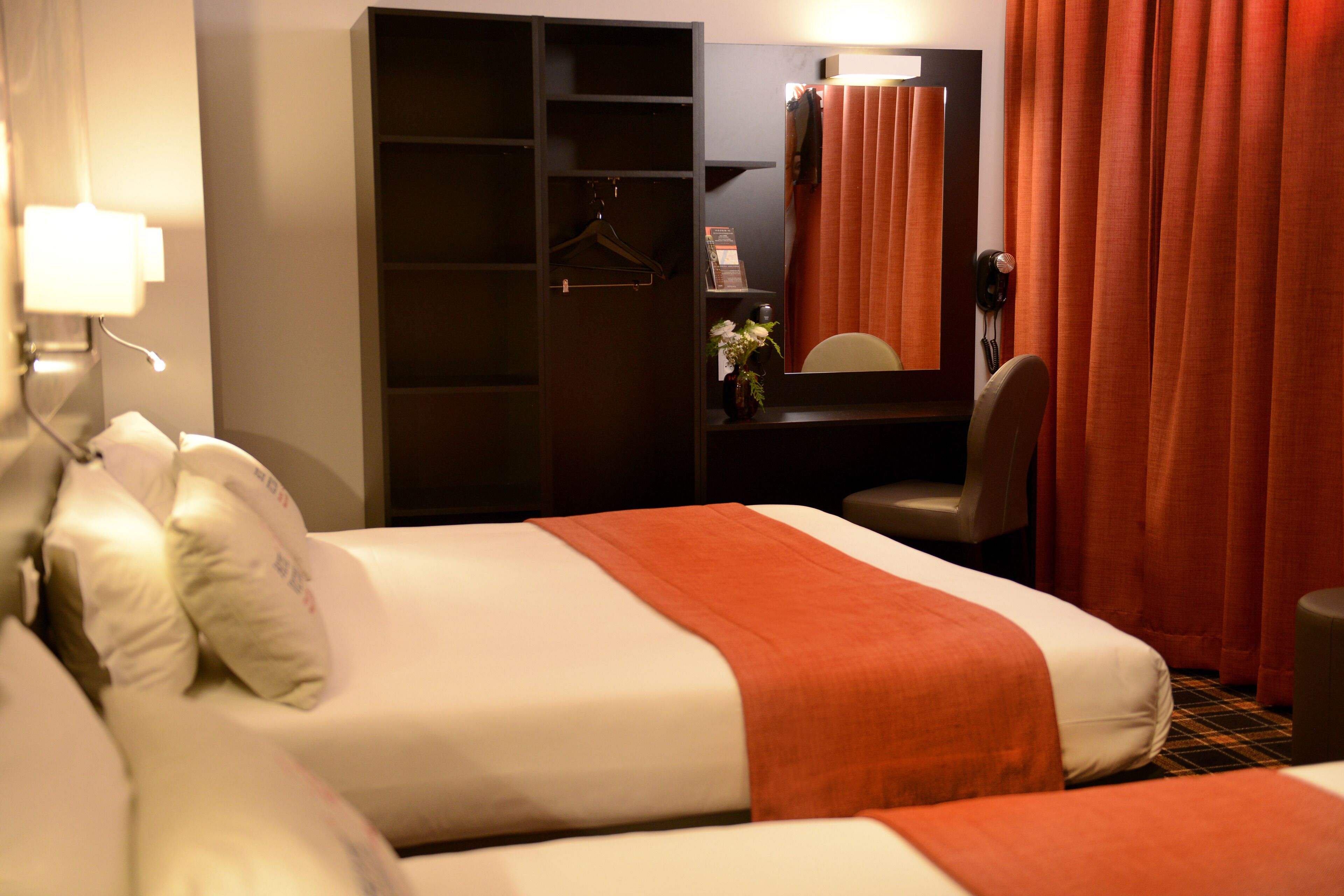 Une chambre d’hôtel avec deux lits, une armoire, un bureau avec une chaise et un miroir.