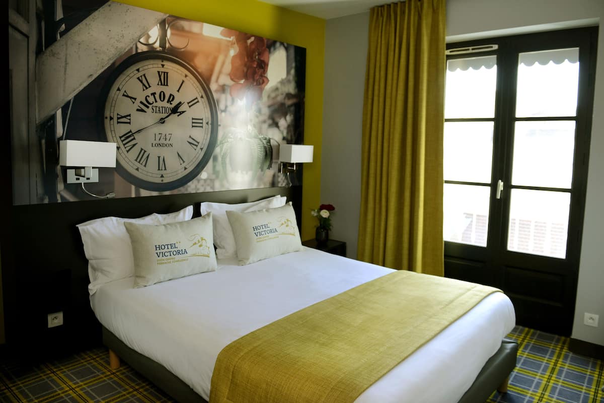 A hotel room with a large bed, a clock on the wall, and a window with curtains.