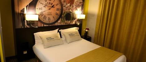 Une chambre d’hôtel avec une grande horloge murale, deux lampes de chevet et un lit recouvert d’un tapis à carreaux.