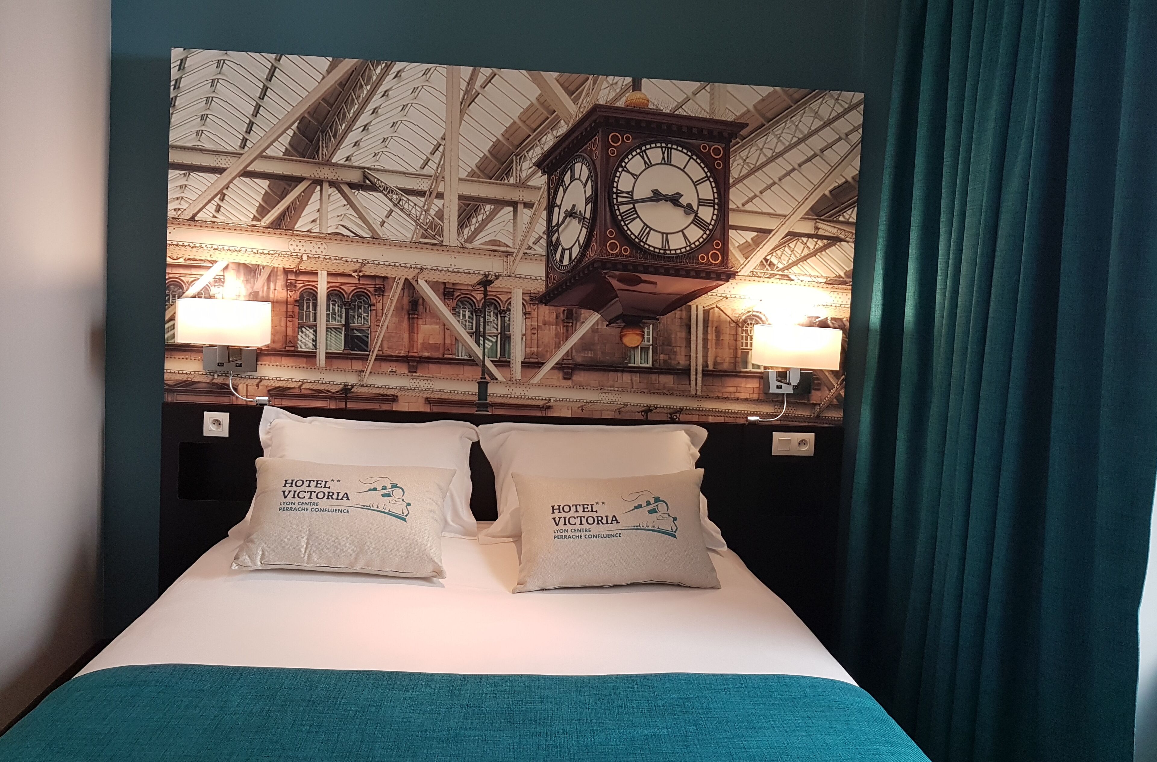 Une chambre d’hôtel avec un lit, des oreillers, une horloge et un mur orné d’une horloge et de lampes.