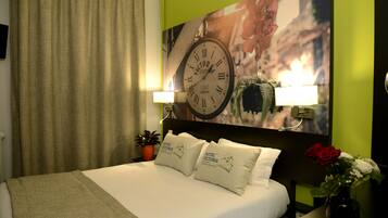 A hotel room with a bed, a clock, a potted plant, and a vase with flowers.