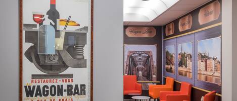 A vintage poster with a train and a bottle, and a seating area with orange chairs and a clock.