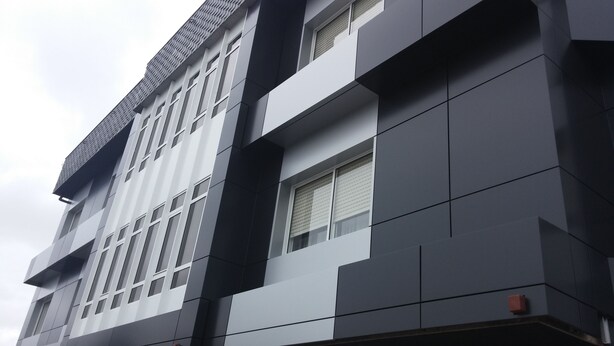 A modern building with a geometric facade, large windows, and a flat roof. - Los Olmos (Lugo)