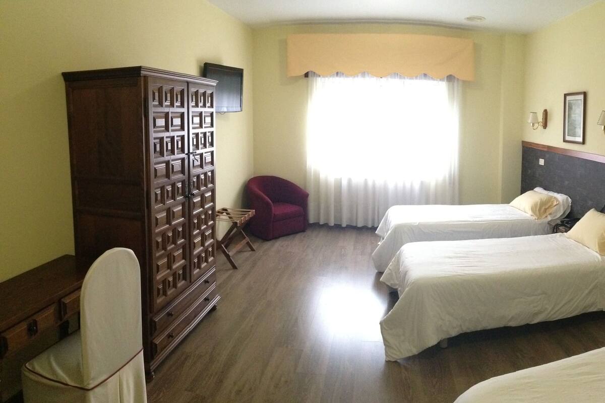 Une chambre d’hôtel avec deux lits simples, une armoire en bois, une chaise rouge et une grande fenêtre avec des rideaux.