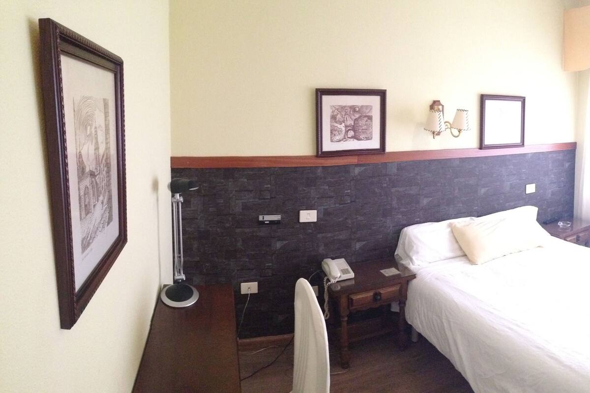 Une chambre d’hôtel équipée d’un lit, d’un bureau, d’une chaise, d’un téléphone et d’une lampe fixée au mur.