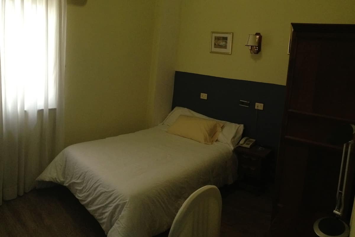 Une chambre d’hôtel avec un lit, une table de chevet, un téléphone, un tableau au mur et une porte.