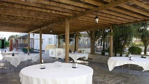 An outdoor patio with round tables covered in white tablecloths, wooden pergola overhead, and stone flooring. - Los Olmos (Lugo)