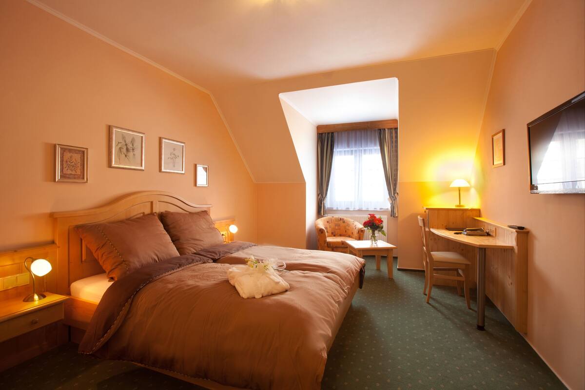 A hotel room with a large bed, a desk, a chair, and a television.