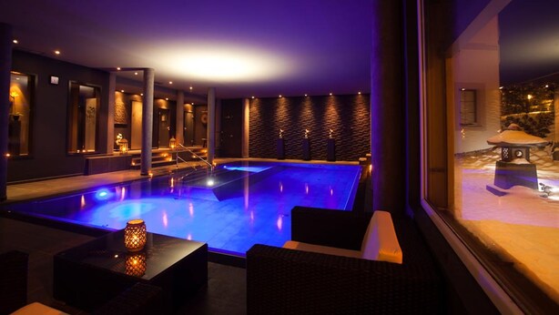 Un área de piscina interior moderna con iluminación azul, asientos y vistas al exterior.
