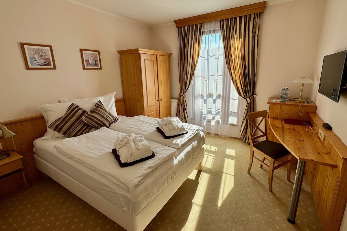 A hotel room with a bed, a desk, a chair, a TV, and curtains.