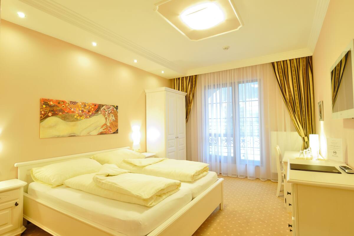 A hotel room with a large bed, a desk, a wardrobe, and a painting on the wall.