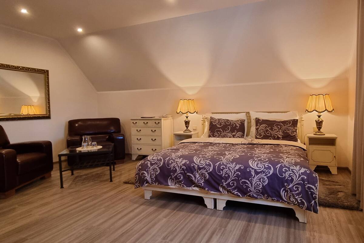 A bedroom with a bed, two bedside tables, a dresser, a chair, a mirror, and a ceiling light fixture.