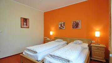 A hotel room with two single beds, a wooden headboard, bedside tables with lamps, and two framed pictures on the orange wall.