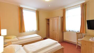 A hotel room with two single beds, a wooden wardrobe, a desk with a chair, and a television.