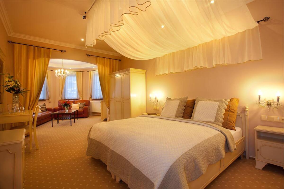 A spacious bedroom with a large bed, a sitting area with a sofa, and a chandelier.