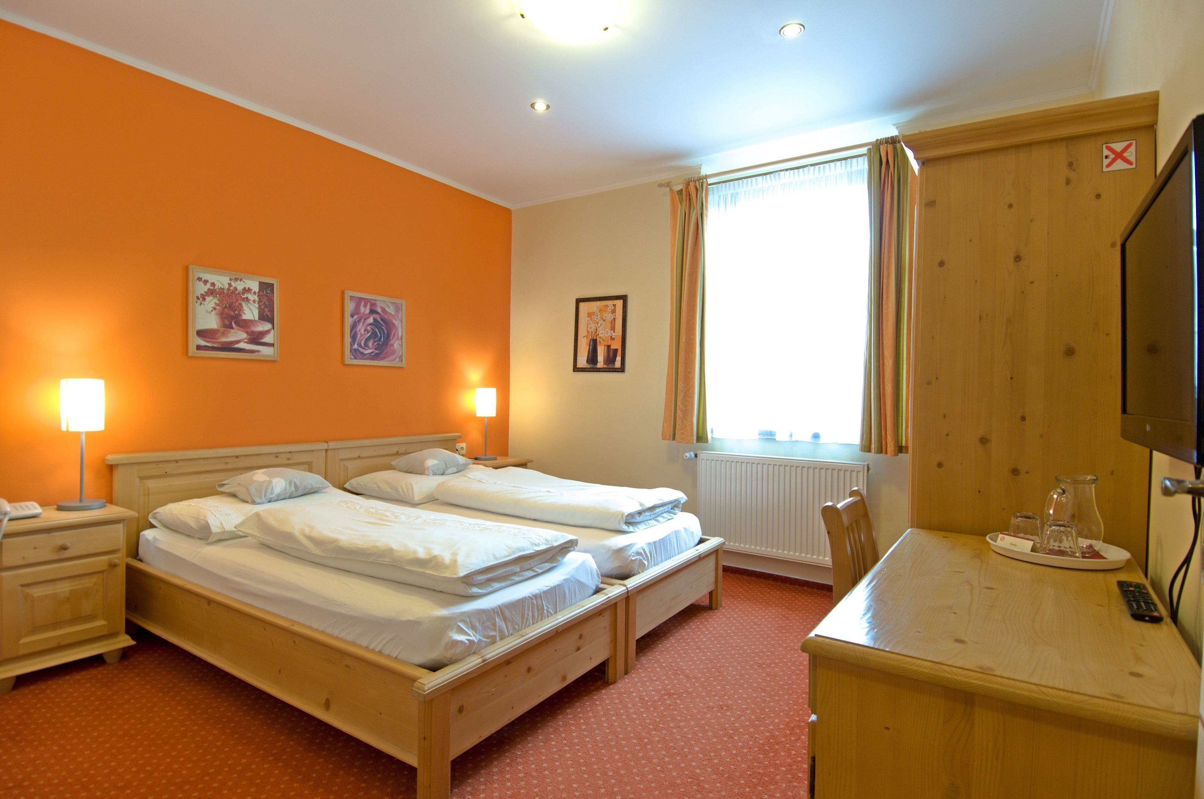 Une chambre d’hôtel avec deux lits, un bureau avec une chaise, une télévision et des œuvres d’art accrochées aux murs.