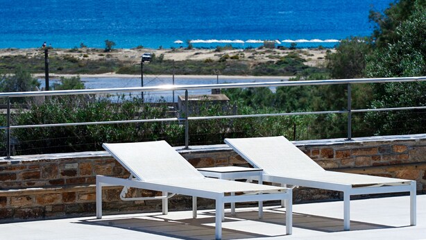Un área de piscina con dos sillas reclinables blancas, un muro de piedra y vistas al mar y la playa.