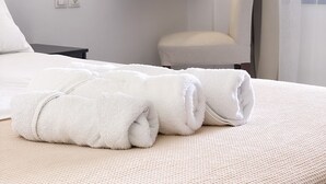 Una habitación de hotel moderna con una cama bien hecha, una silla, un espejo montado en la pared y una mesita de noche con lámpara.