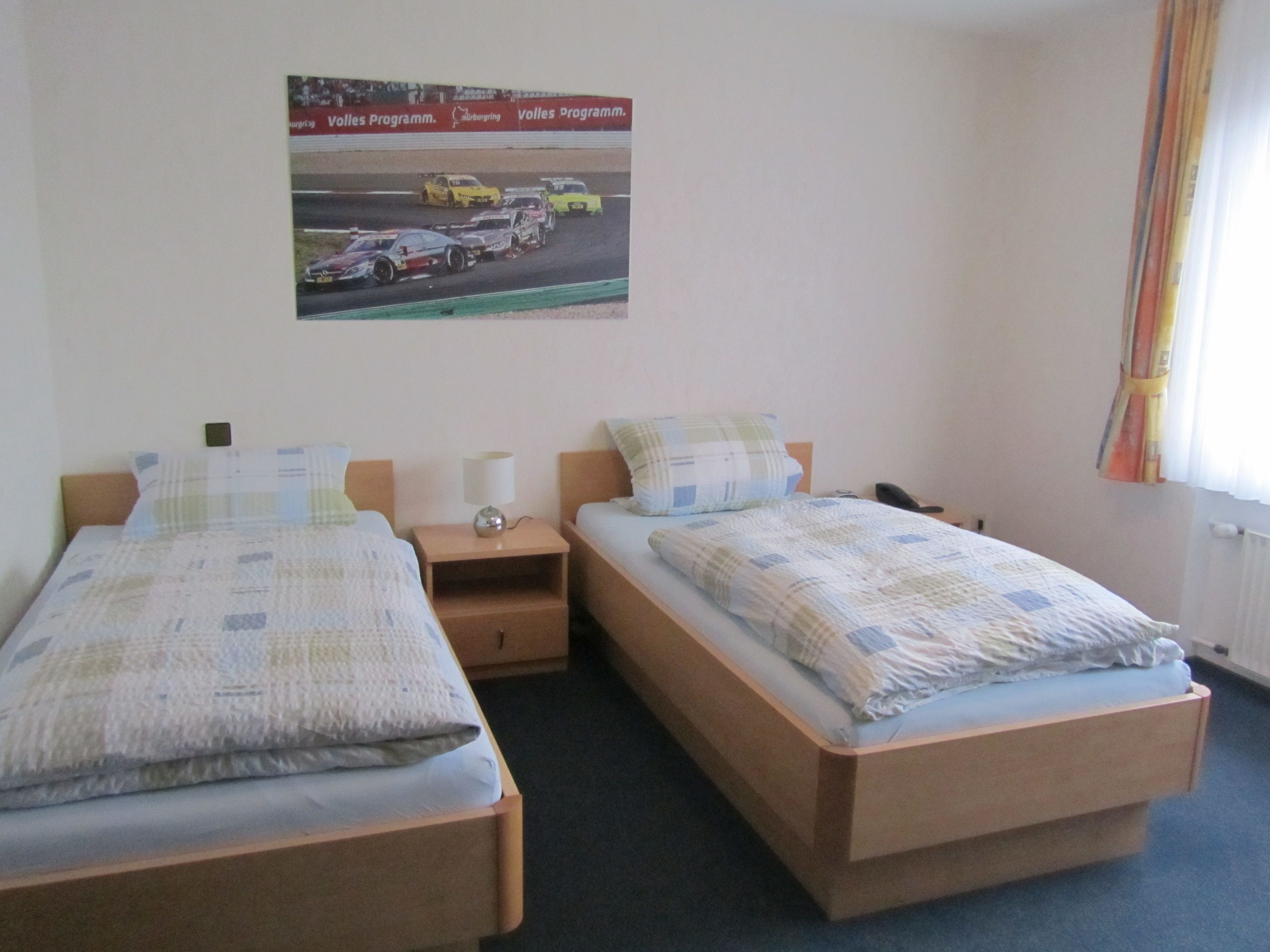 Ein Hotelzimmer mit zwei Betten, einem Nachttisch mit Lampe, einem Telefon und einem Poster einer Rennveranstaltung an der Wand.