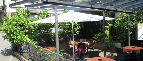 An outdoor patio area with tables and chairs, covered by a transparent roof structure.