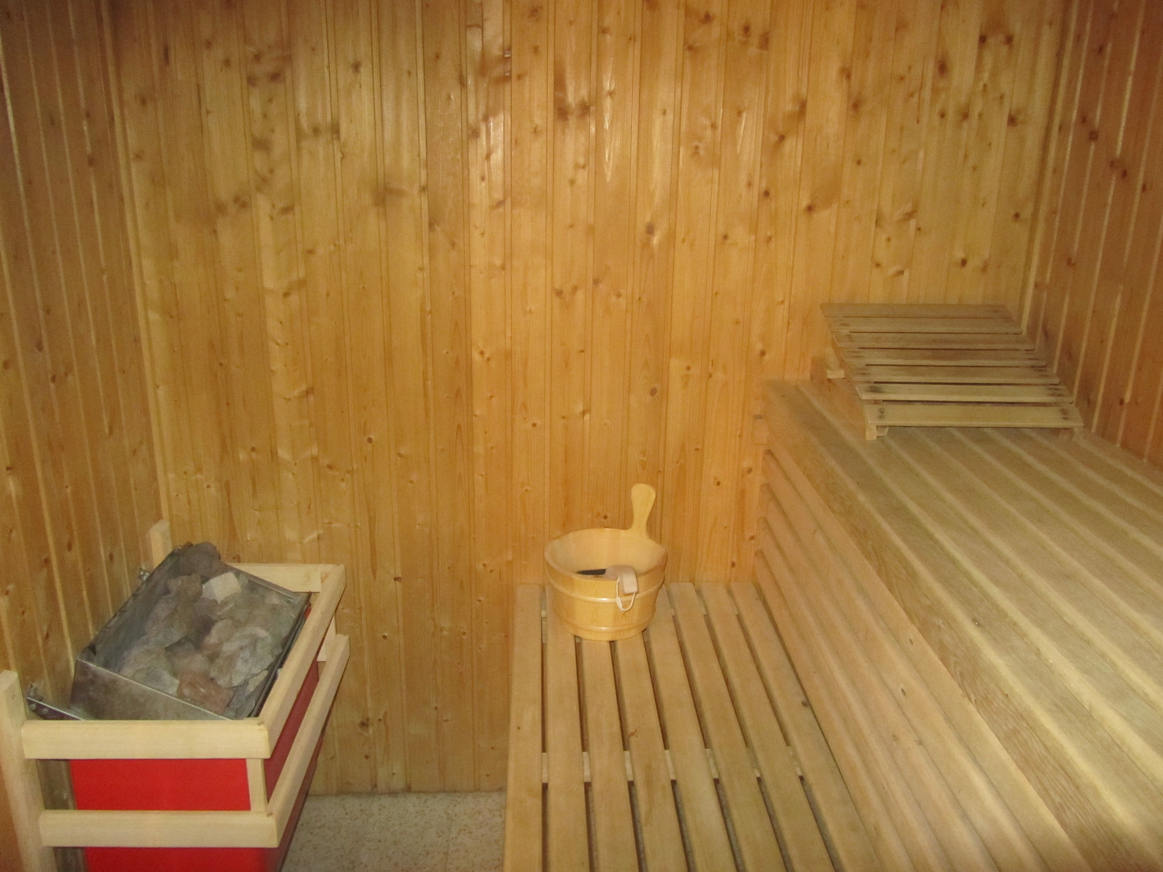 A sauna room with wooden walls, a wooden bench, and a small wooden basin.