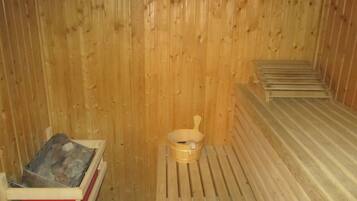 A sauna room with wooden walls, a wooden bench, and a small wooden basin.