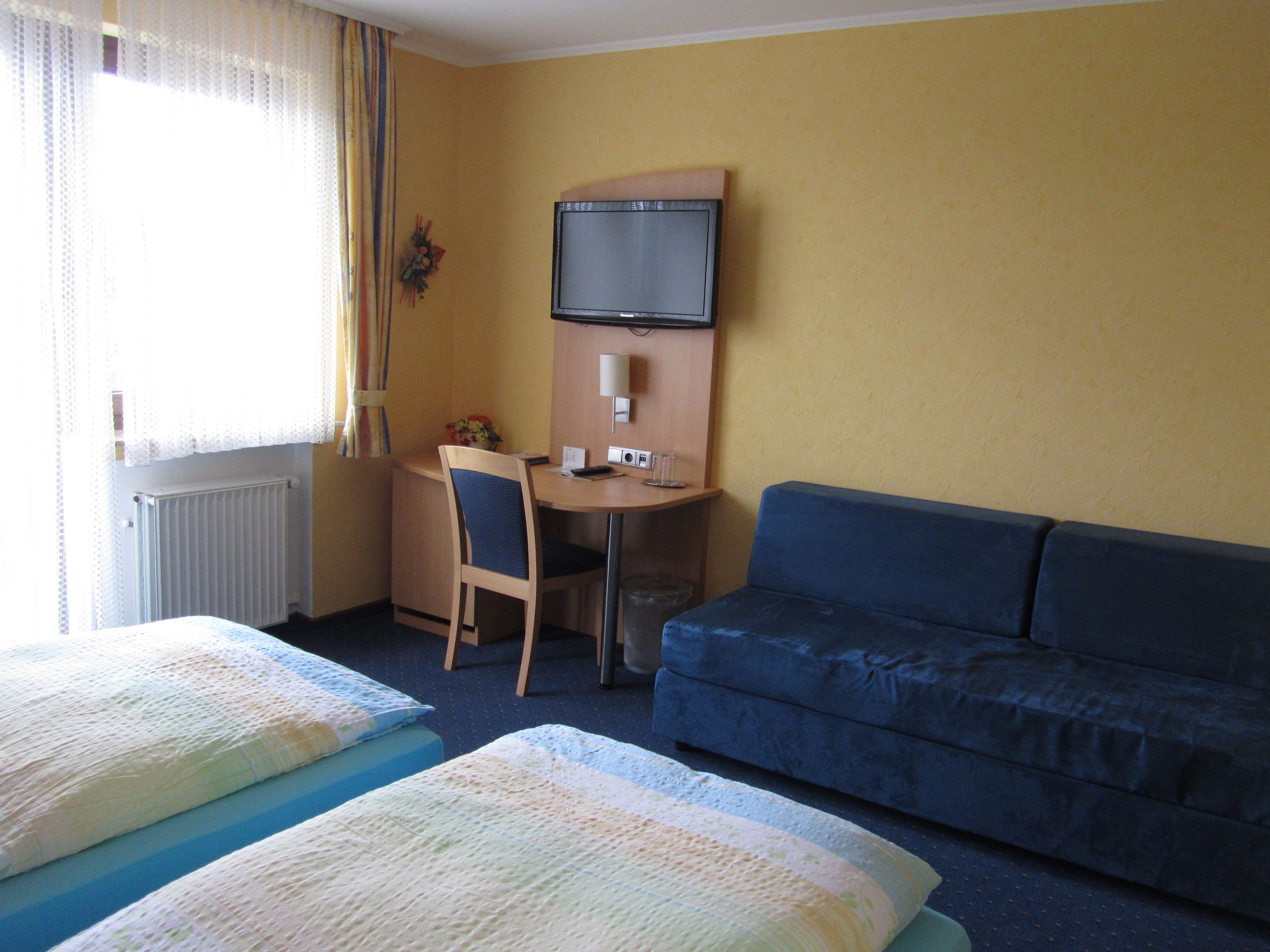 A hotel room with two beds, a desk, a chair, a television, and a sofa.