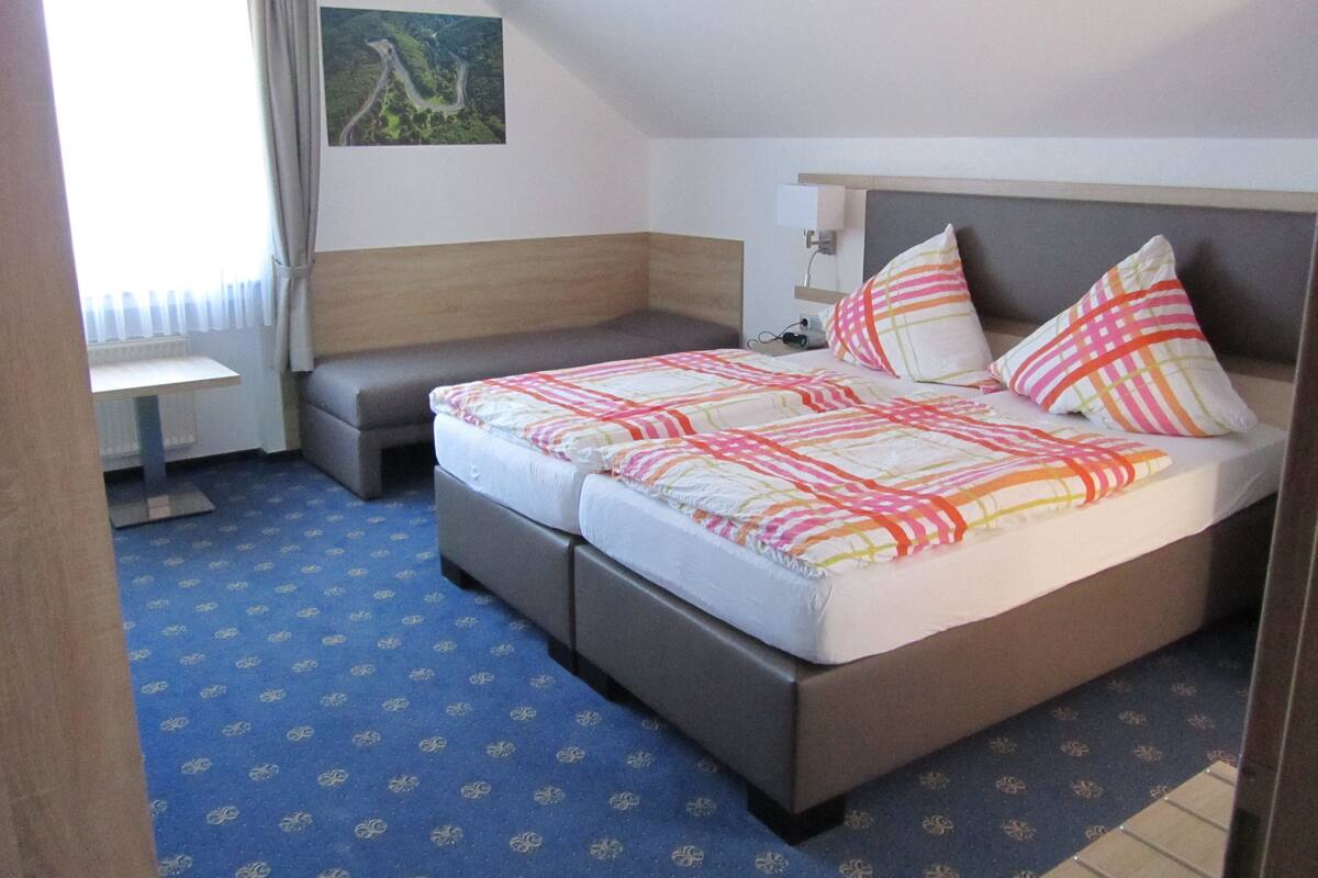Ein Hotelzimmer mit einem Doppelbett, einem kleinen Schreibtisch und einem Fenster mit Vorhängen.