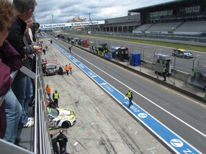 A race track with a blue and white advertising banner, a yellow car, and several people in safety vests. - Race-Hotel zur Burg Nürburg (Nuerburg)