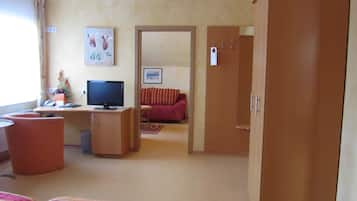 A hotel room with a bed, a desk with a computer, a television, a red sofa, and a wardrobe.