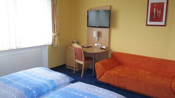 Een hotelkamer met twee bedden, een bureau, een stoel, een oranje bank, een televisie en een lijst aan de muur.