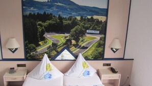 A hotel room with a bed, two bedside tables, a lamp, a painting of a landscape, and a telephone.