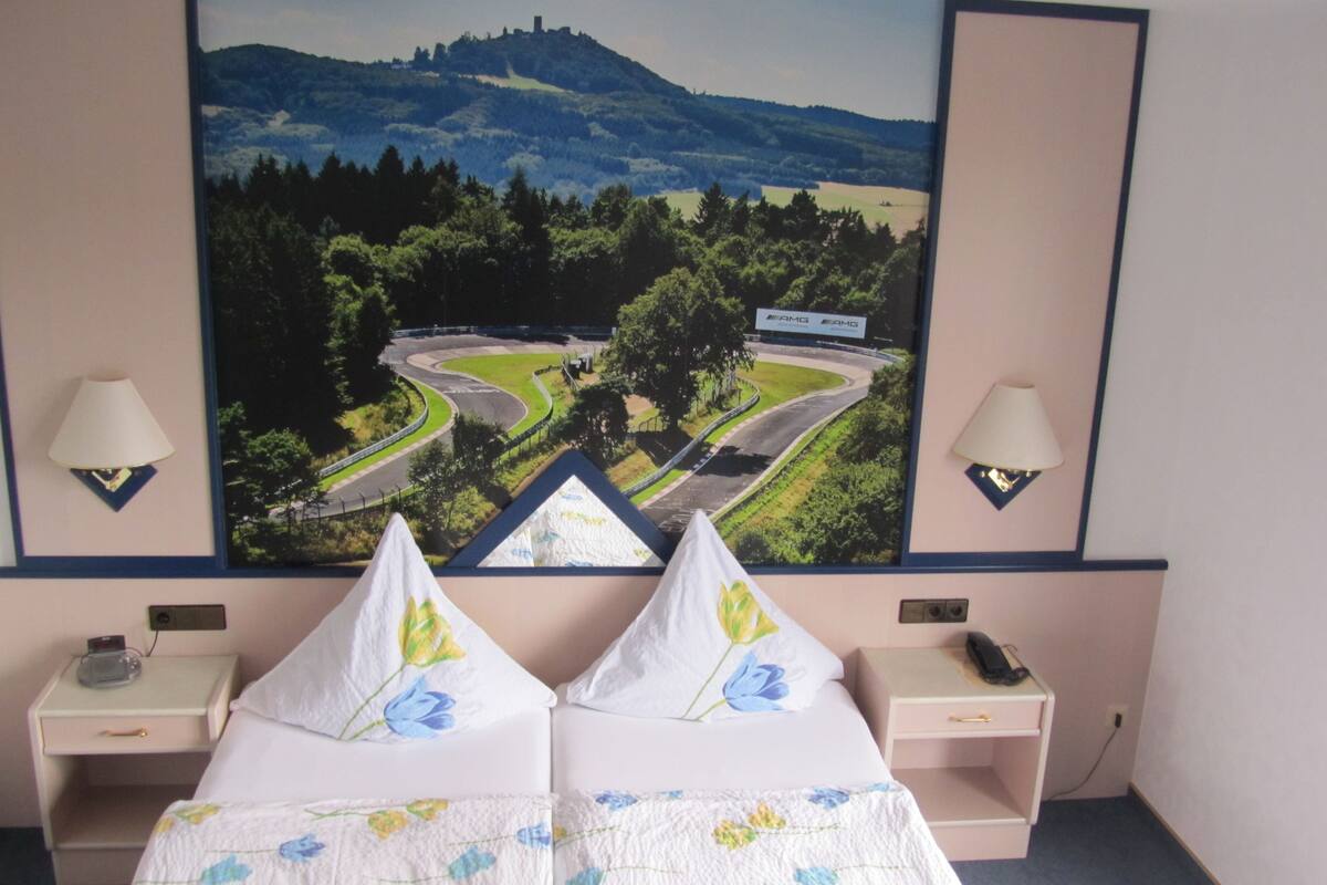 Ein Hotelzimmer mit einem Bett, zwei Nachttischen, einer Lampe, einem Landschaftsbild und einem Telefon.