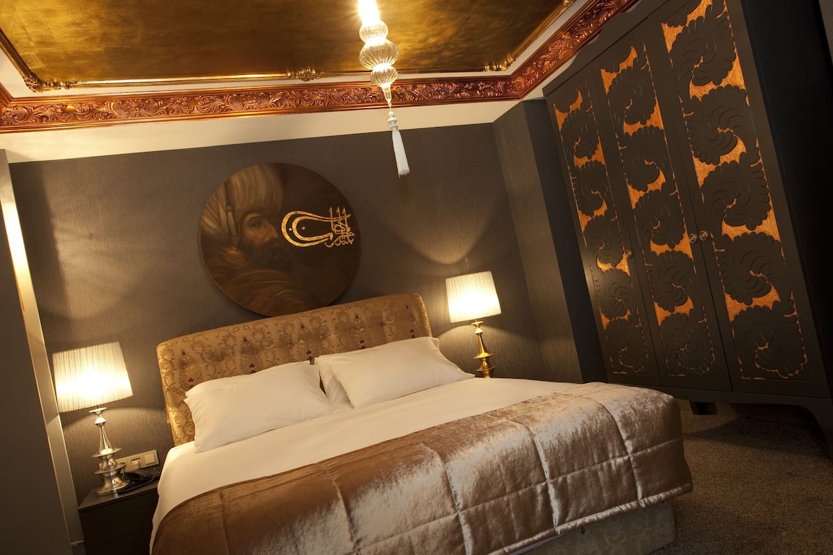 A well-appointed hotel room with a large bed, two bedside lamps, a decorative wall piece, and a wardrobe with intricate patterns.