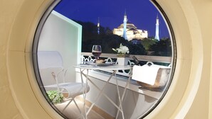 A round window with a view of a building with two minarets and a dome, a table with chairs, and a potted plant.