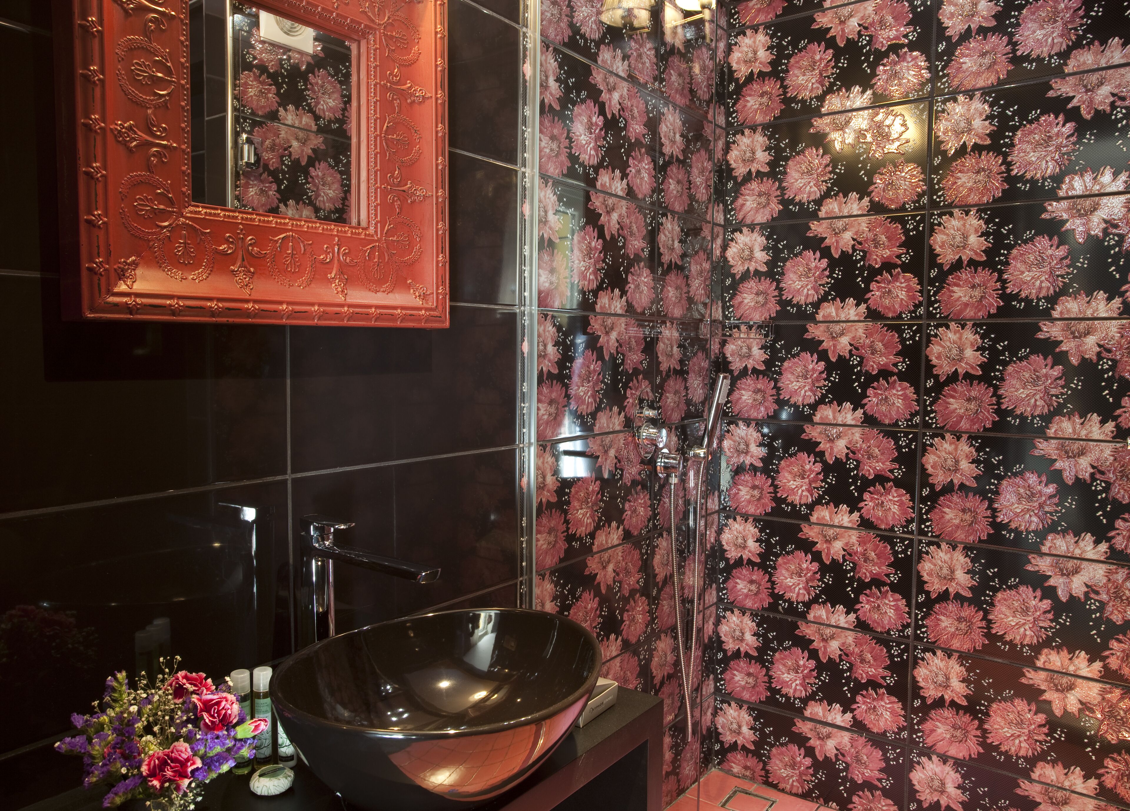 A bathroom with a large black sink, a mirror, and a wall with a floral tile pattern.