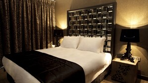 A hotel room with a large bed, zebra-patterned curtains, a headboard with mirrored panels, a bedside table with a lamp, and a decorative wooden nightstand.