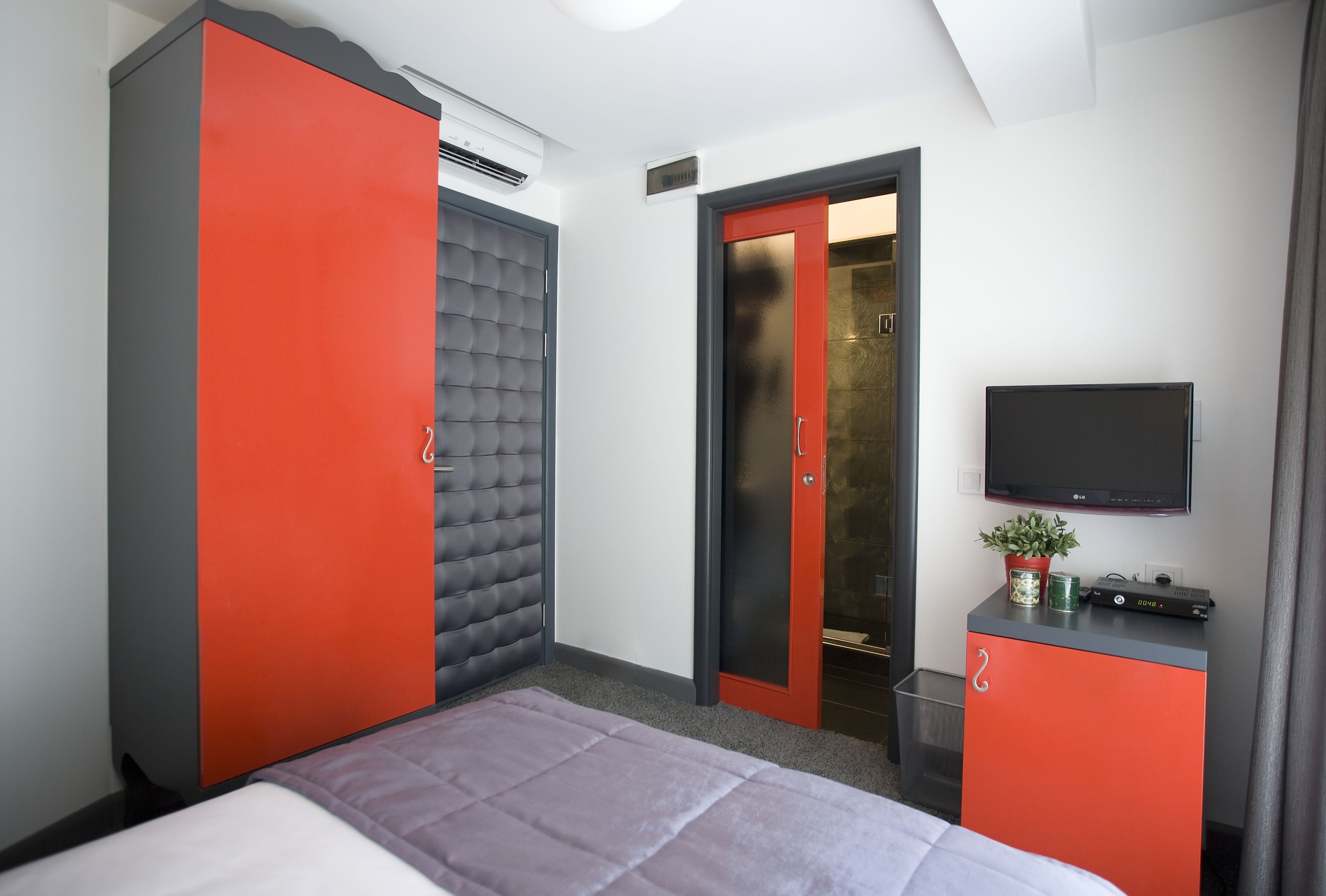 A hotel room with a bed, a wardrobe, a television, and a small table with a plant.