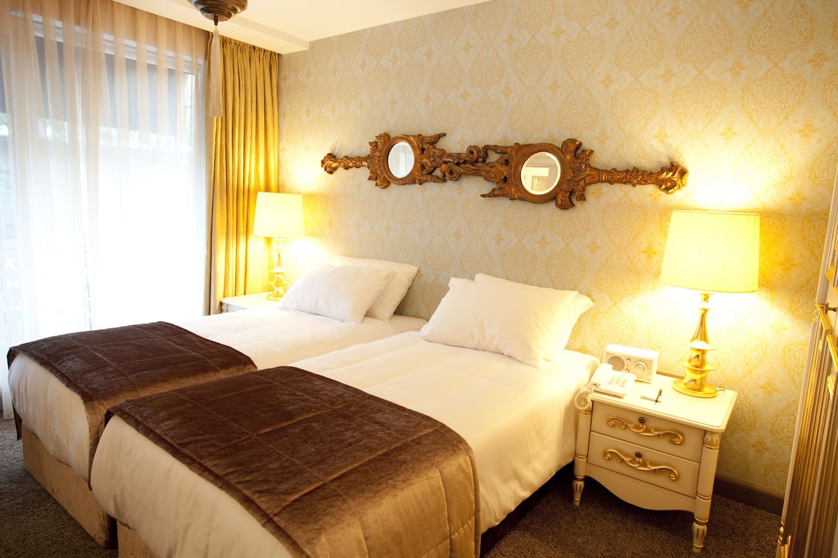 A hotel room with two beds, a nightstand with a lamp, and a mirror on the wall.