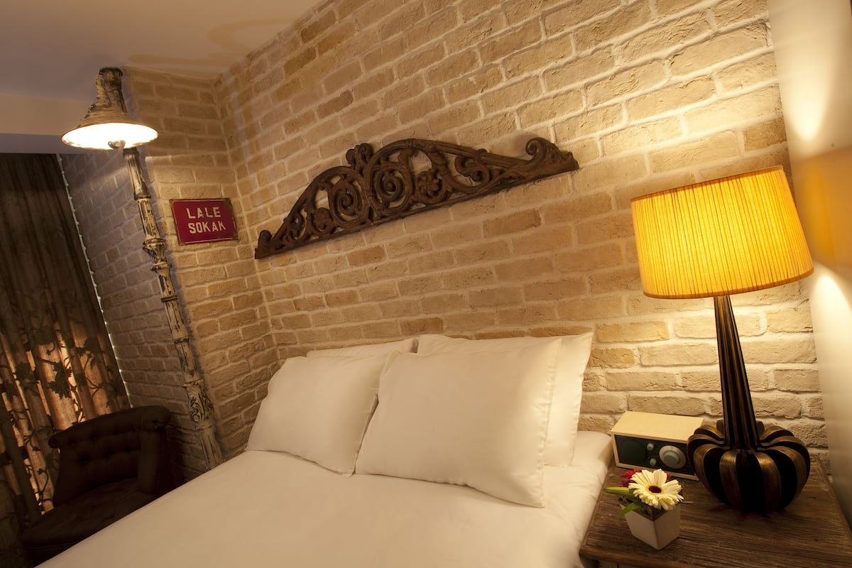A room with a bed, a nightstand with a lamp, a vintage radio, and a sign on the wall.